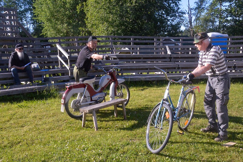 Kesäteatterin näyttämön nurmikolla kaksi miestä mopon ja polkupyörän kanssa