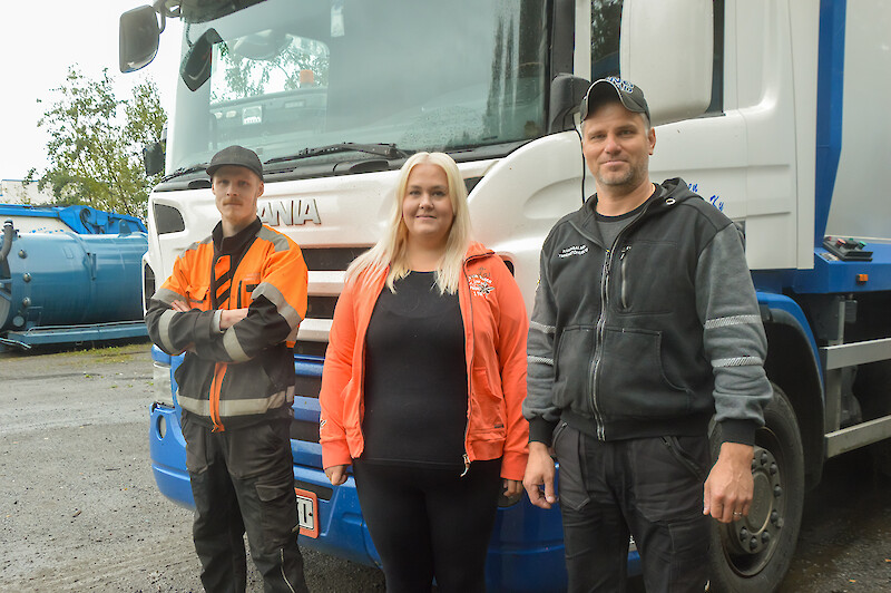 Kolme henkilöä jäteauton edessä